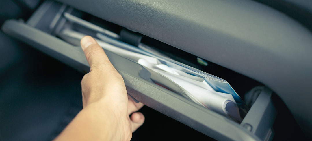 Mano abriendo la guantera de un coche con documentos