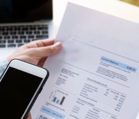 Persona sosteniendo un documento y un smartphone con un ordenador de fondo