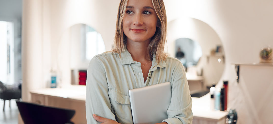 Chica joven en una peluquería abrazando una tablet y con cara emocionada